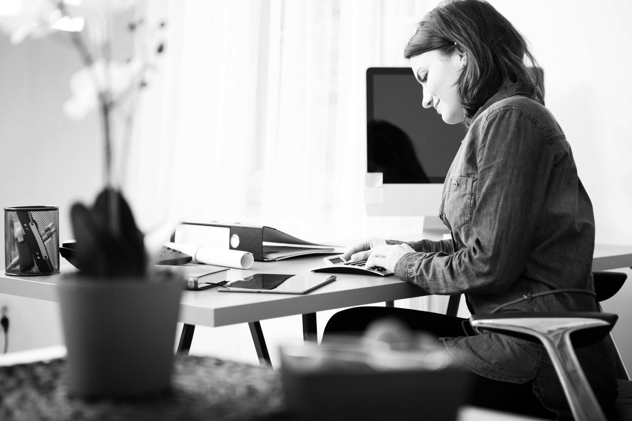 Busy Pretty Young Businesswoman in Denim Blouse Sitting at her Worktable with Documents and Electronic Devices.